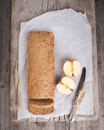 Auf dem Foto ist das Apfel-Kürbis-Brot zu sehen, daneben liegen Äpfel und Getreide. | © SONNENTOR
