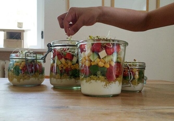 Salat im Glas | © SONNENTOR Auf dem Foto sieht man mehrere Gläser mit buntem Salat geschichtet. Jemand streut gerade noch Sprosse darauf. | © SONNENTOR