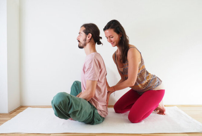 Yoga Schmetterling | © SONNENTOR Auf dem Foto sieht man einen Mann in der Yogaposition Schmetterling. Seien Yogapartnerin unterstütz seinen Rücken. | © SONNENTOR