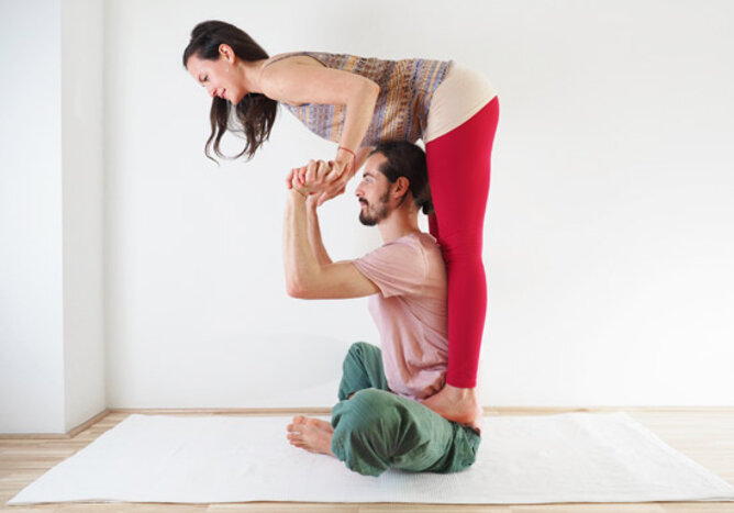 Yoga Partnerübung Schmetterling | © SONNENTOR Auf dem Foto sieht man wie zwei Yogapartner den Schmetterling ausführen. | © SONNENTOR
